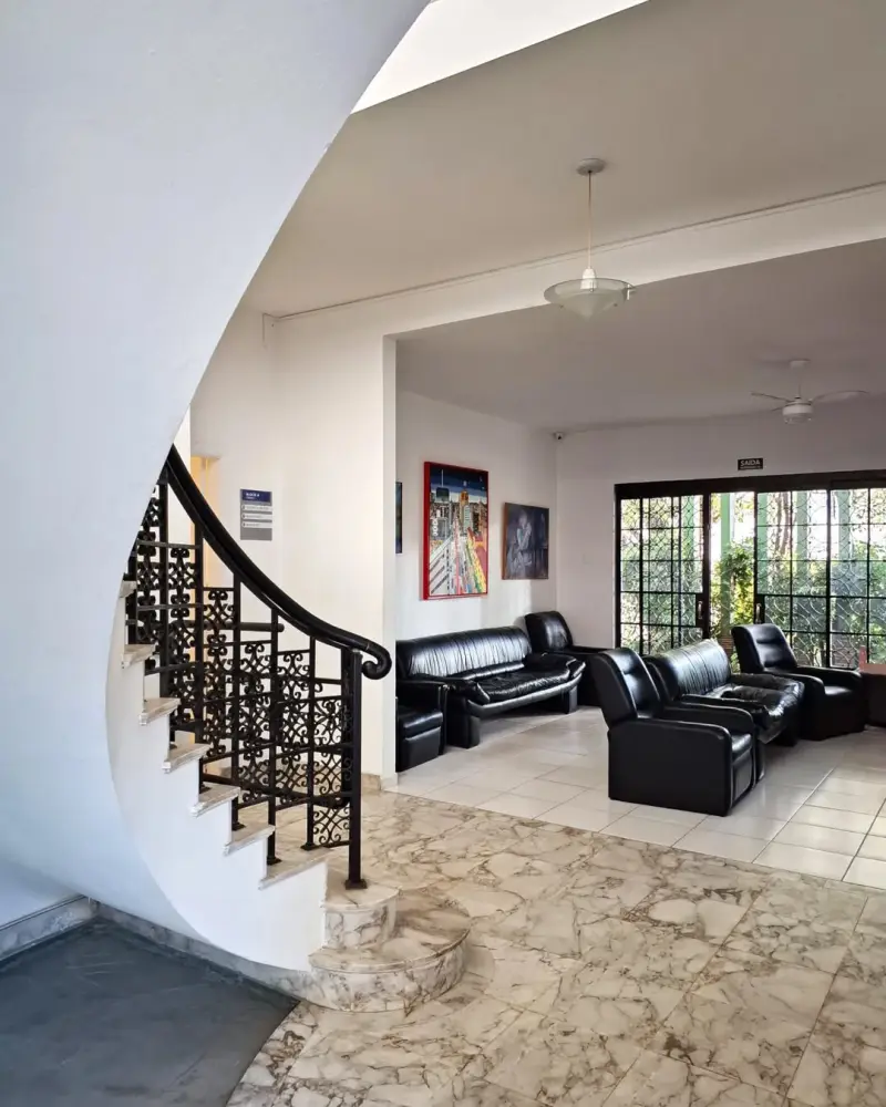 Sala de estar do casarão com escada em curva, guarda-corpo de ferro e piso de mármore