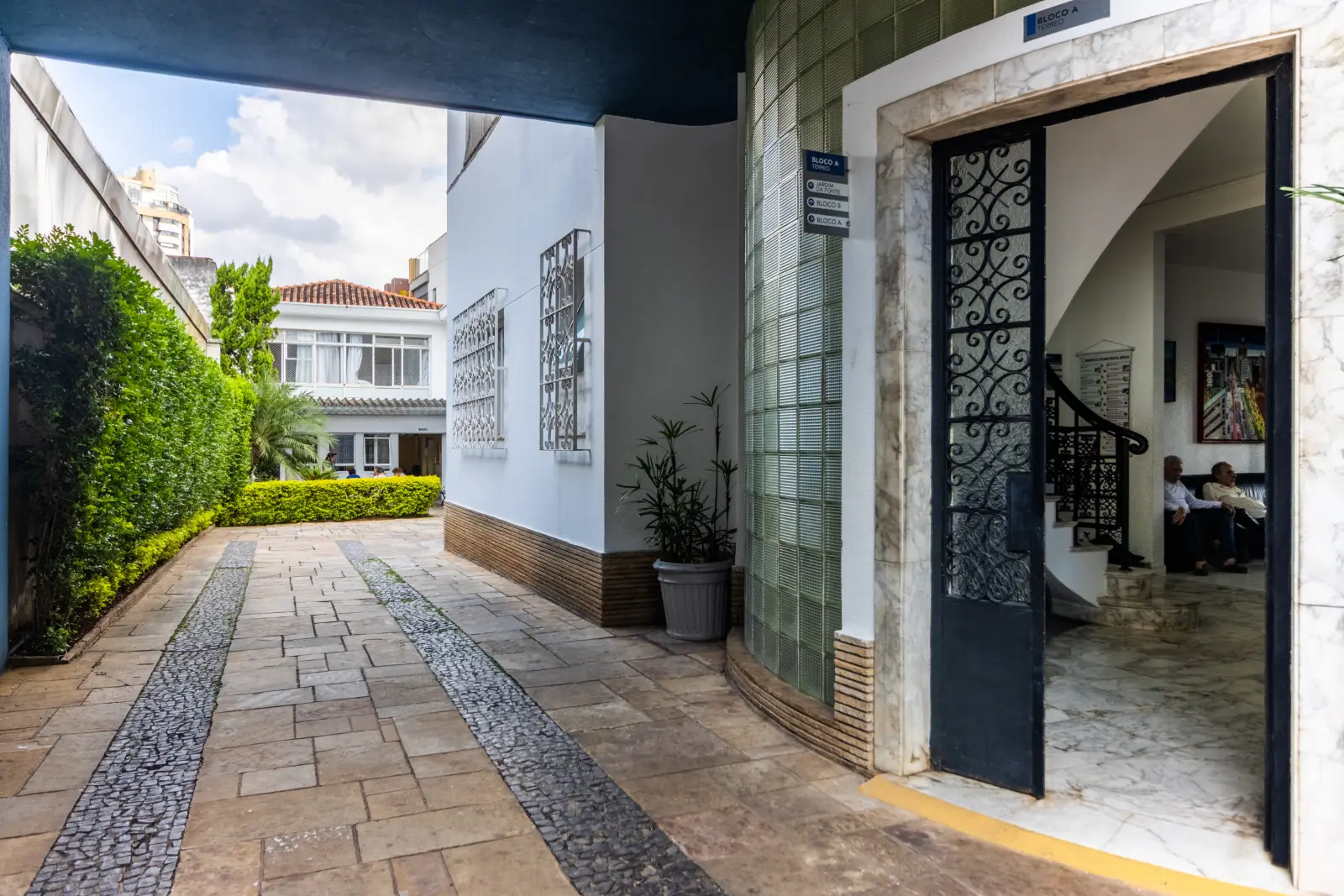 Entrada da Mental Sênior com piso de pedra, jardim e porta de ferro trabalhado