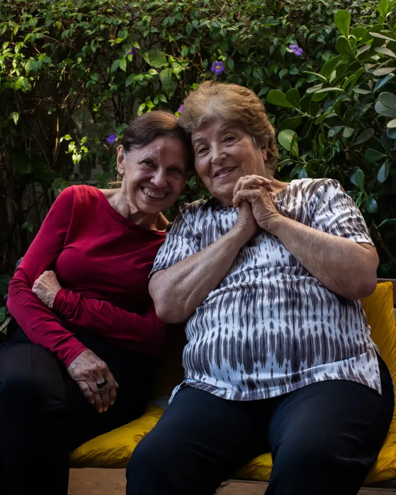 Duas residentes sorridentes abraçadas em um banco do jardim